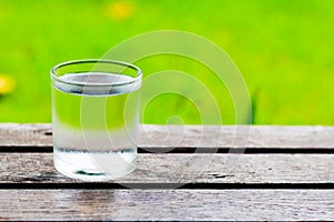 Cool water glass on wooden table with grass field background.