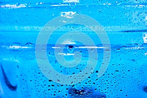 Cool water and water drops on a blue plastic bottle . Selective focus.