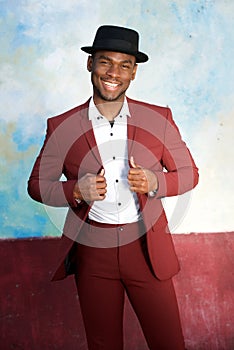 Cool young african american male fashion model smiling with hat and vintage suit by wall