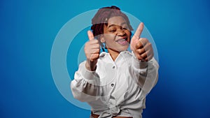 Cool young afro woman showing thumbs up, approves something, blue background