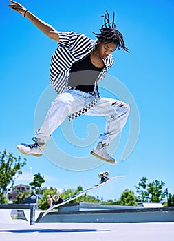 Cool young boy performing tricks on his skateboard at the skatepark. Focused young African American man jumping to flip