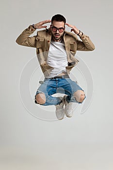 Cool young casual guy in jacket jumping and pointing fingers to head