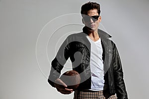 cool young footballer in leather jacket holding american football ball