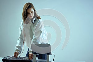 Cool young girl DJ mixes music on a mixing console and laptop, in stylish clothes, on white blue background.