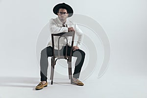 cool young man with hat holding arm on chair's back and sitting