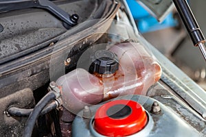 Coolant tank stained with oil with a level sensor and wires electricians in the engine compartment of the car in the workshop for