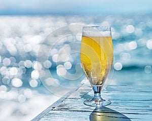 Cooled glass of beer on the blue wooden table. Blurred sea is at the background