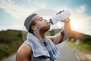 Cooling off after an intense run. a sporty young man drinking water while exercising outdoors.