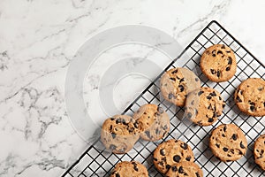 Cooling rack with chocolate chip cookies on marble background, top view