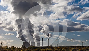 Dark side of steam clouds and smoke of cooling towers and chimneys of a brown coal power plant against the bright sky
