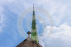 Copper art deco church spire and Celtic cross on top of church against beautiful cloudy blue sky