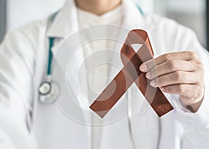 Copper Brown Awareness Ribbon on doctorÃ¢â¬â¢s hand, symbolic color for Anti-Tobacco, Colon Colorectal Cancers, Herpes Simplex Virus photo