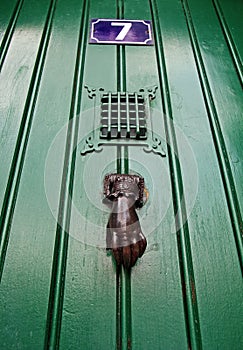 Copper door knocker in a shape of palm is on green wooden door