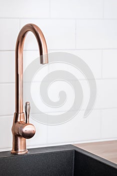 Copper faucet over black modern sink in kitchen