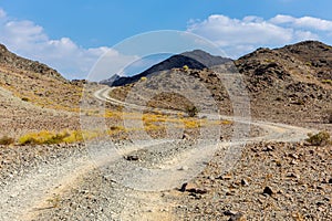 Copper Hike trail, winding gravel dirt road through Wadi Ghargur riverbed and rocky limestone Hajar Mountains in Hatta, UAE