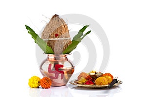 Copper Kalash with coconut and mango leaf and pooja thali with diya, kumkum and sweets with floral decoration on a white photo