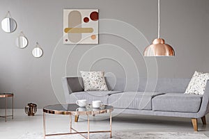 Copper lamp and coffee table in front of a modern sofa in a grey living room interior