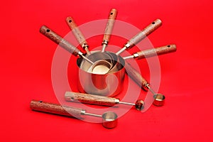 Copper measuring cups spoons with a wooden handle in sets of different sizes on a red background