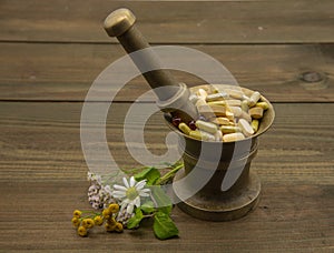A copper mortar full of capsules and pills. Nearby lie medicinal flowers