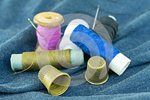 Copper old thimbles, colorful threads and needles on blue fabric