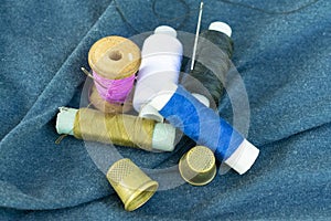 Copper old thimbles, colorful threads and needles on blue fabric