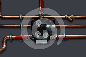 Copper pipes and thermoregulator with valves on a grey wall