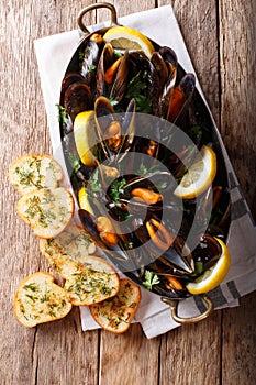 Copper pot of gourmet mussels with lemon, parsley and garlic served on a bread. Vertical top view