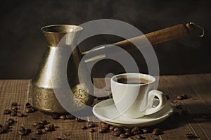 Copper pot and hot coffee cup/copper pot and hot coffee cup on a wooden table with dark background