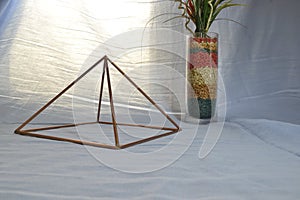 Copper pyramid with lighting, with antique glass vase and stones in side view, with natural background lighting