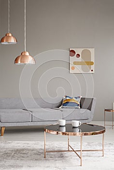 Copper table and lamps in a grey living room interior. Real photo