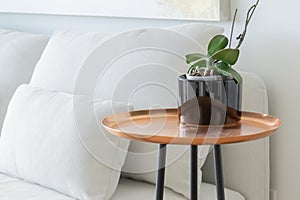 Copper tray side table, with black legs, next to a white futon couch, focused in the distance, with an orchid potted plant