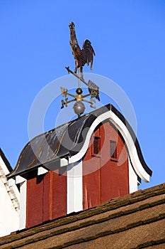 Copper weathervane on red barn cupola, blue sky background.