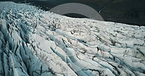 Copter fly over the ice ridge in Iceland. Close-up aerial view of white glacier Vatnajokull with black ash.