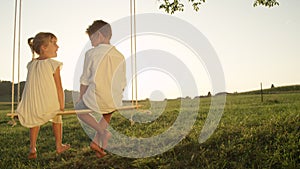 COPY SPACE: Cheerful young children sitting on swing on a warm gold evening
