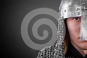 Copy space close Portrait of a medieval warrior of the Viking age in a helmet and chain mail on a dark background. Knight in armor