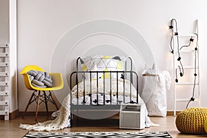 Copy space on empty white wall in classy scandinavian kid`s bedroom with single metal bed, yellow chair and paper bag with pillow