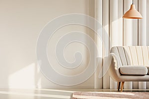 Copy space on empty white wall of fashionable living room with pastel orange lamp and white sofa in the corner