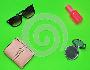 Copy space of female fashion accessories layout on a green background. Mirror, sunglasses, purse, perfume bottle. Top view