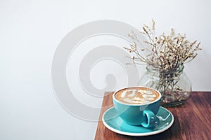 Copy space image of a blue cup of hot latte coffee and dry flowers in a vase on vintage wooden table