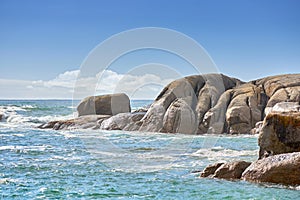 Copy space at sea with a cloudy blue sky background and rocky coast in Camps Bay, Cape Town, South Africa. Boulders at a