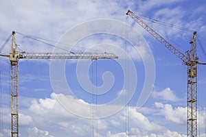 Copy space between two construction cranes against blue cloudy sky