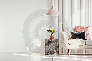 Copy space on white wall of elegant living room with white flowers on glass vase on stylish table next to white sofa