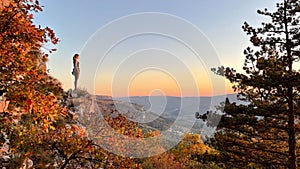 COPY SPACE: Young woman rock climbing observes the sunset from top of a cliff.