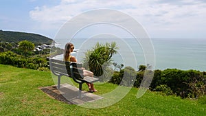 COPY SPACE: Young woman sits on a bench and looks at the exotic nature and ocean