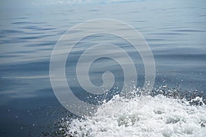 Copyspace scene of gradient blue sea light ripple background with white bubble foam water splashing by running boat