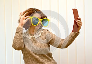 The coquettish woman in big sunglasses smiles, looking at herself in a mirror