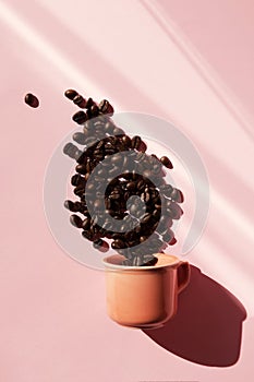 Coral colored cup with effuse coffee`s beans with shadows on pastel rose background. Flat lay. Top view. Coffee concept. Pop art