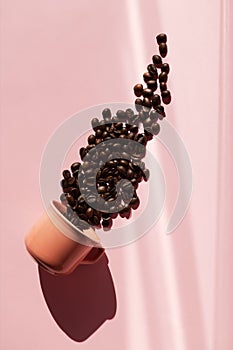 Coral colored cup with effuse coffee`s beans with shadows on pastel rose background. Flat lay. Top view. Coffee concept. Pop art