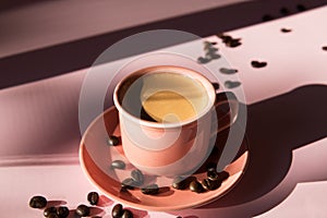 Coral colored cup with effuse coffee`s beans with shadows on pastel rose background. Flat lay. Top view. Coffee concept. Pop art