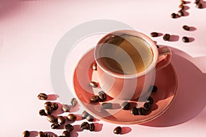 Coral colored cup with effuse coffee`s beans with shadows on pastel rose background. Flat lay. Top view. Coffee concept. Pop art